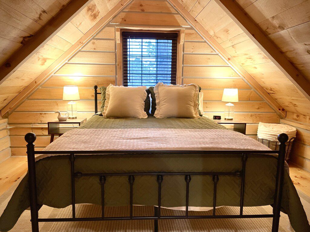 🛏️ Retreat to Upstairs Bedroom #1—queen bed, soft linens, fluffy pillows, and a USB outlet on the nightstand for charging. The perfect log cabin haven for a restful night’s sleep! 🌙🔌