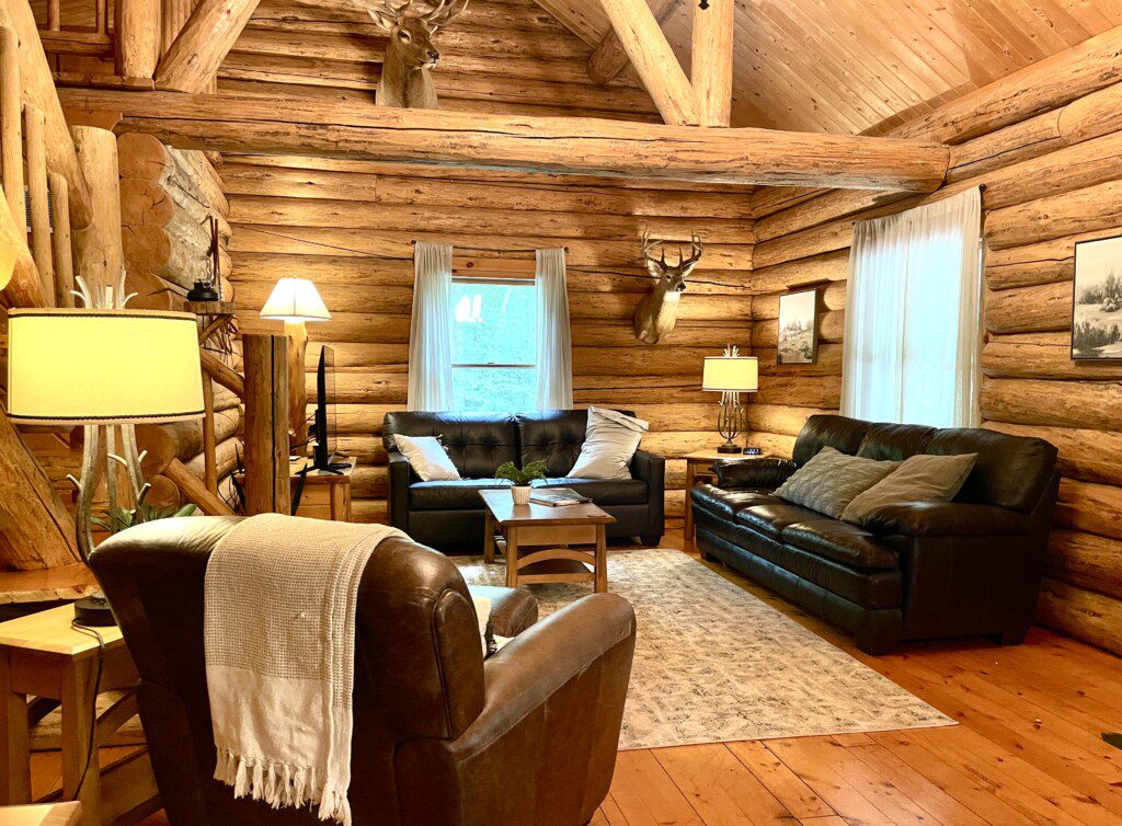 Cozy up in the rustic charm of Trillium Lane Cabin’s open-concept living room, featuring warm log interiors, inviting leather seating, nature-inspired decor, and a 50" Roku Smart TV for your entertainment
