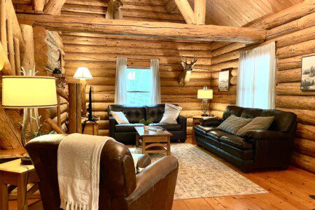 Cozy up in the rustic charm of Trillium Lane Cabin’s open-concept living room, featuring warm log interiors, inviting leather seating, nature-inspired decor, and a 50" Roku Smart TV for your entertainment