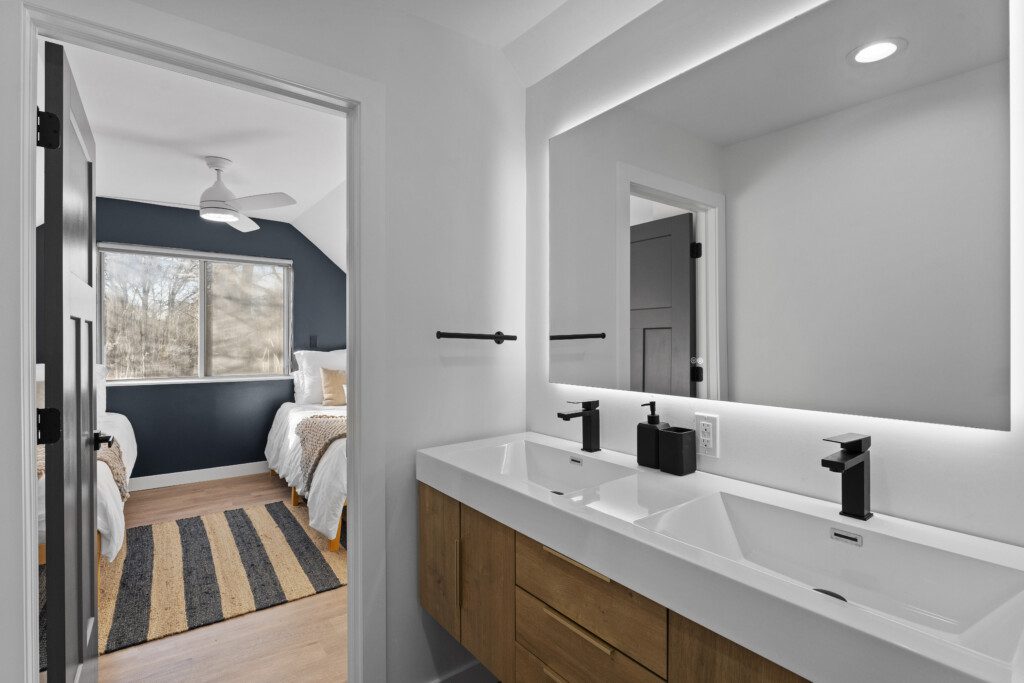 Bathroom 3 (Upstairs) – Modern full bath featuring a spacious walk-in shower with sleek tile, double vanity with backlit mirror, and stylish black fixtures.