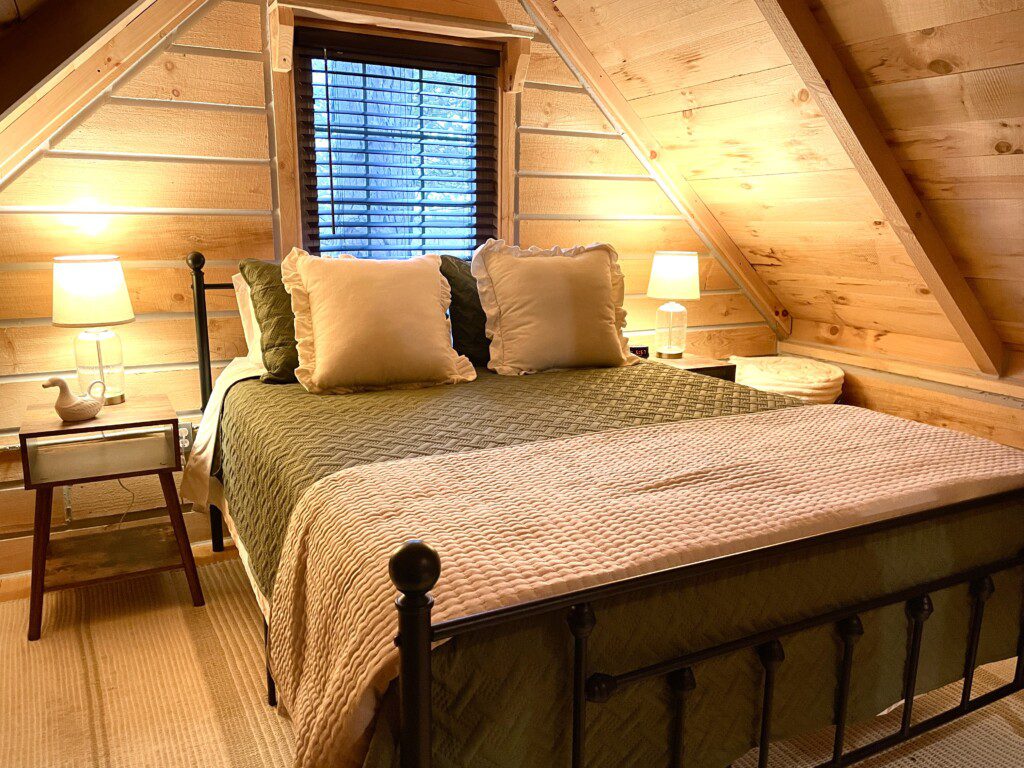 🛏️ Retreat to Upstairs Bedroom #1—queen bed, soft linens, fluffy pillows, and a USB outlet on the nightstand for charging. The perfect log cabin haven for a restful night’s sleep! 🌙🔌