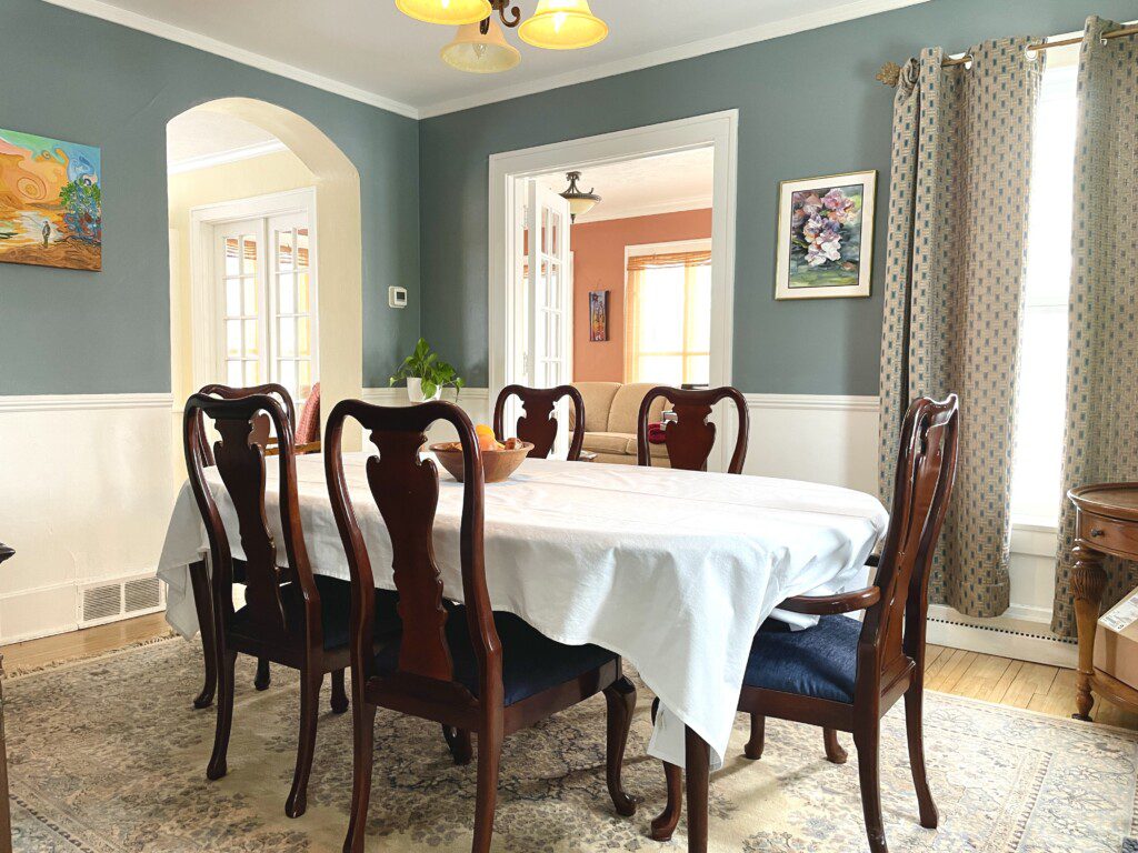 Elevate your mealtime into an occasion 🍽️🌿 — gather around this elegantly set dining room with a crisp tablecloth, classic wood chairs, and lush greenery for a meal that feels truly special.