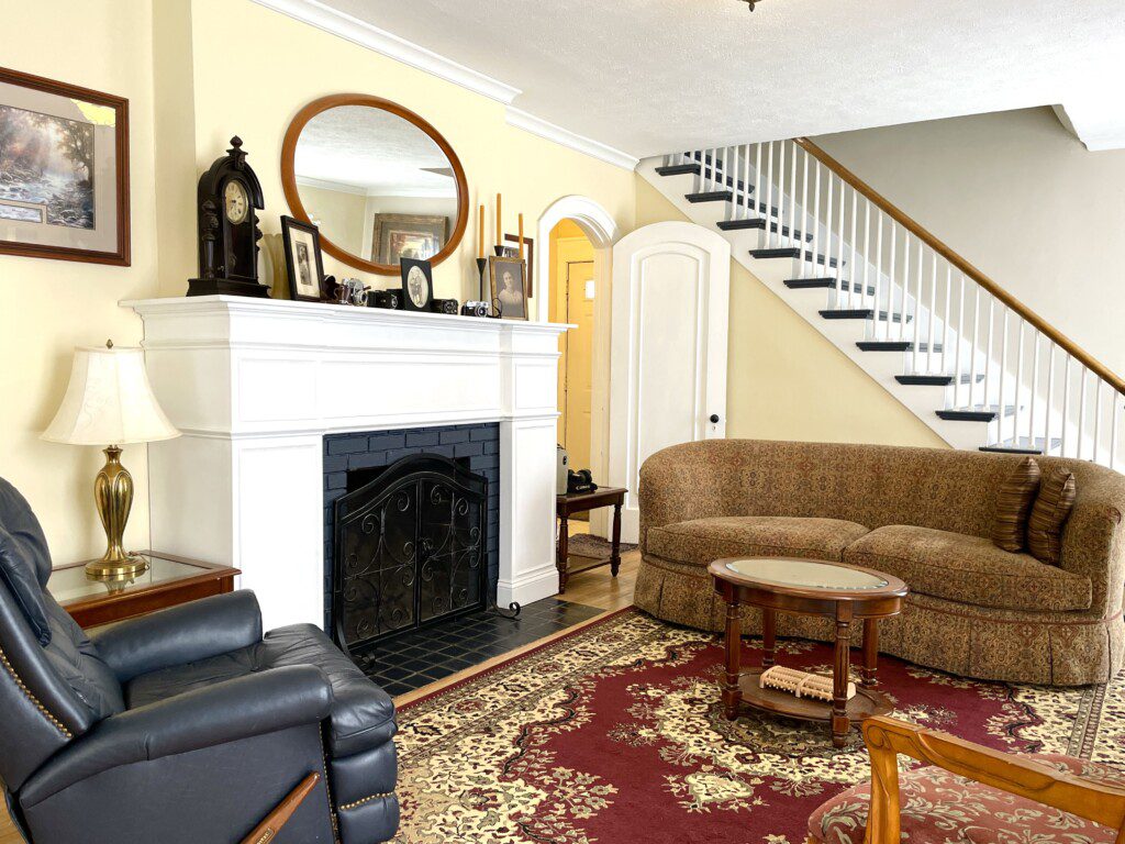 Gather by the fire and feel completely at home 🔥🛋️ — this stunning living room with its elegant white fireplace, classic staircase, and warm rug is where your best memories get made.