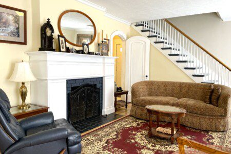 Gather by the fire and feel completely at home 🔥🛋️ — this stunning living room with its elegant white fireplace, classic staircase, and warm rug is where your best memories get made.